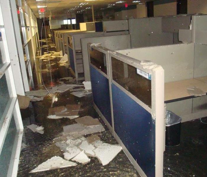 Large office space with standing water and parts of collapsed ceiling on the floor.