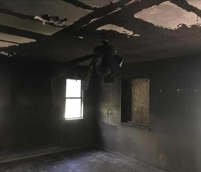 one window boarded, smoke covered walls and ceiling in a home after fire damage