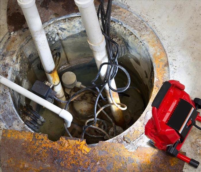 Repairing a sump pump in a basement with a red LED light illuminating the pit and pipe work for draining ground water